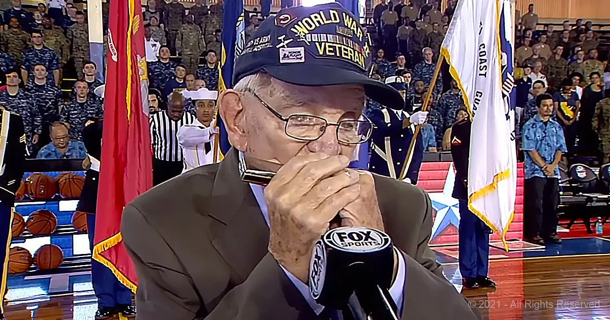 Veteran in "World War II Veteran" hat speaks into Fox Sports microphone at military event.