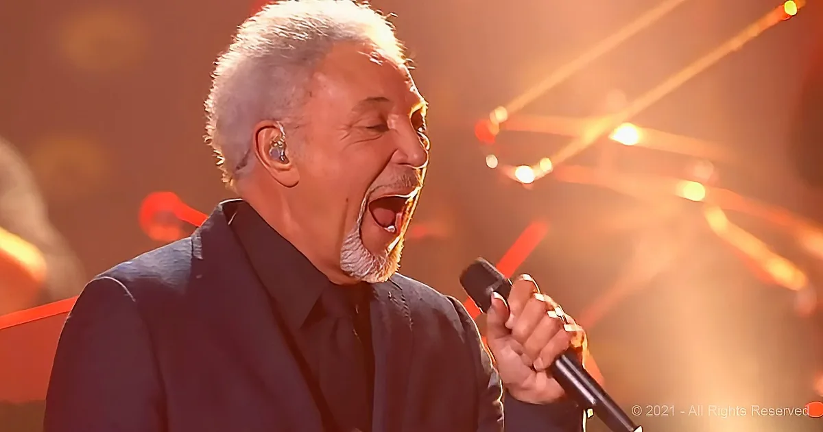 A man with gray hair and beard sings passionately into a microphone on stage.