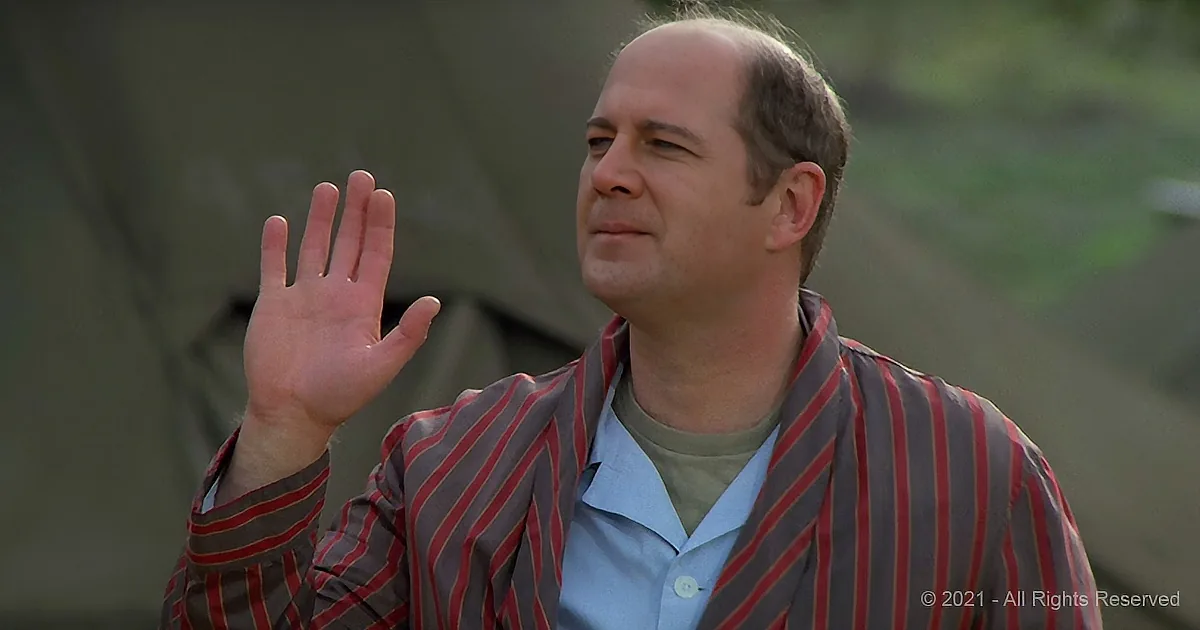 A man in a striped jacket raises his hand, looking upward, with a blurred background.