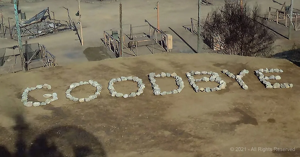 The word "GOODBYE" is spelled out with rocks on a sandy surface.