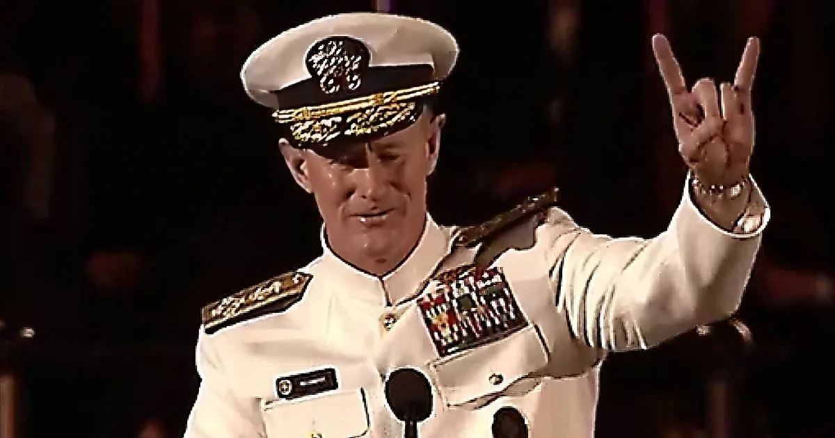 A man in a white military uniform delivers a speech at a podium.
