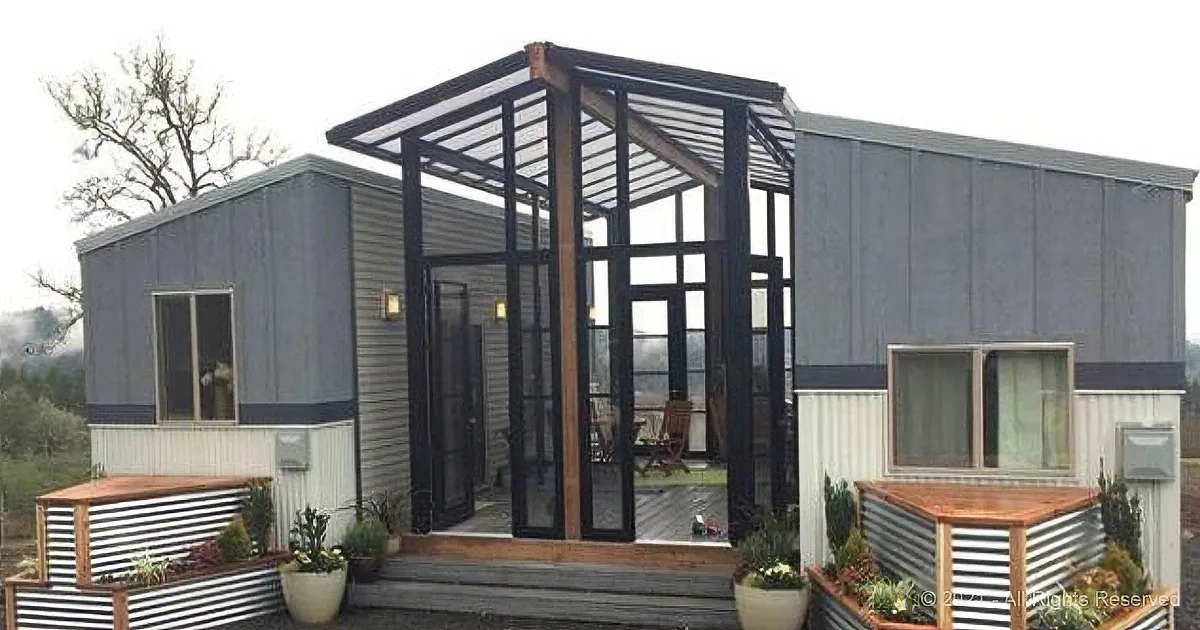 A modern, minimalist house with a large glass front, wooden deck, and corrugated metal siding.