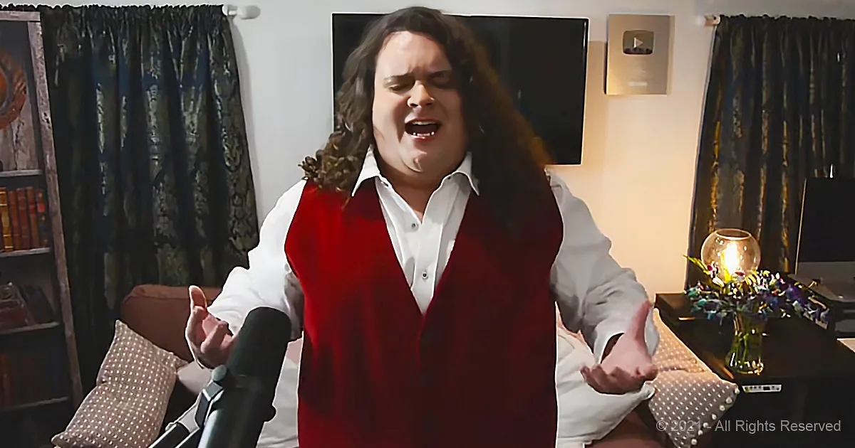 A person in a red vest sings passionately in a cozy room with a microphone, bookshelf, and floral arrangement.