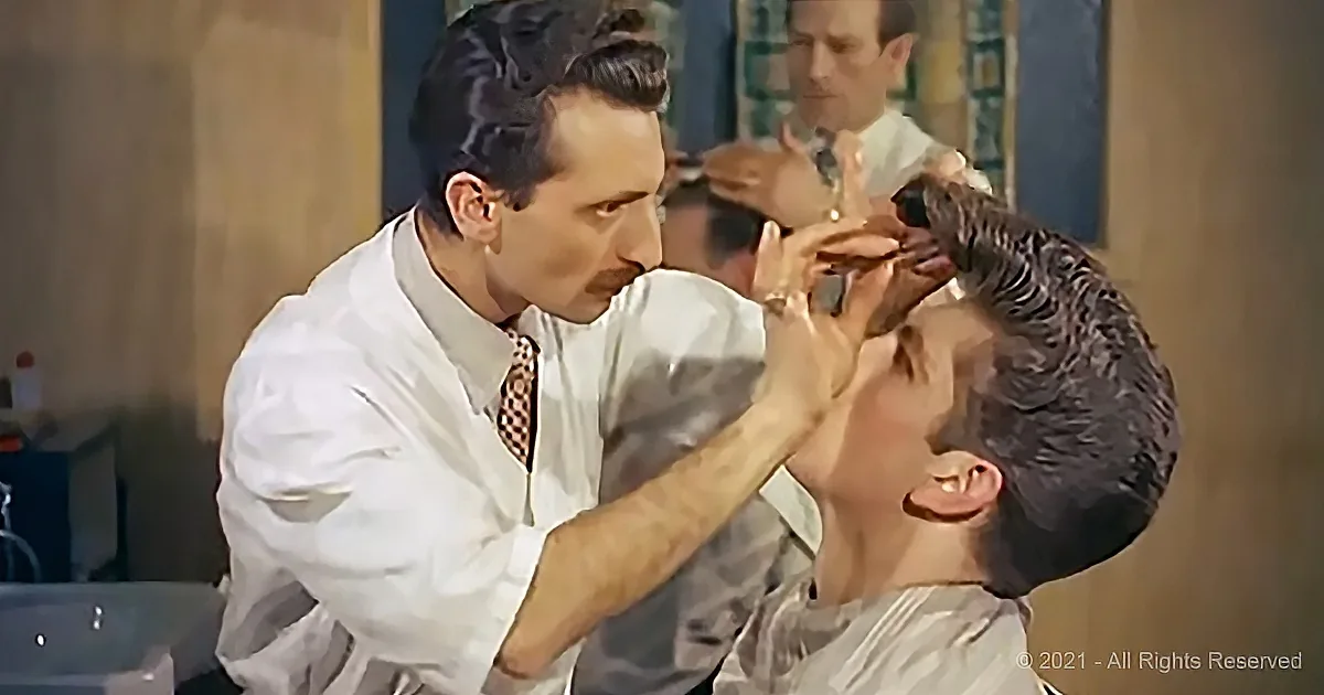 A man in a white shirt and tie is shaving another man's face with a razor in a barbershop.