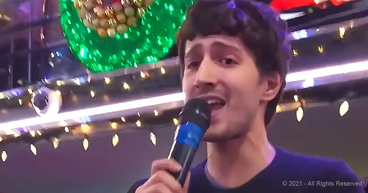 A person holding a microphone, singing, with a festive background of lights and a green ornament.