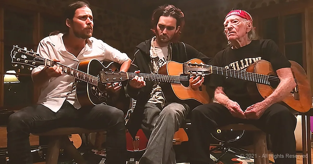 Three men play guitars in a dimly lit room, one wearing a red bandana.