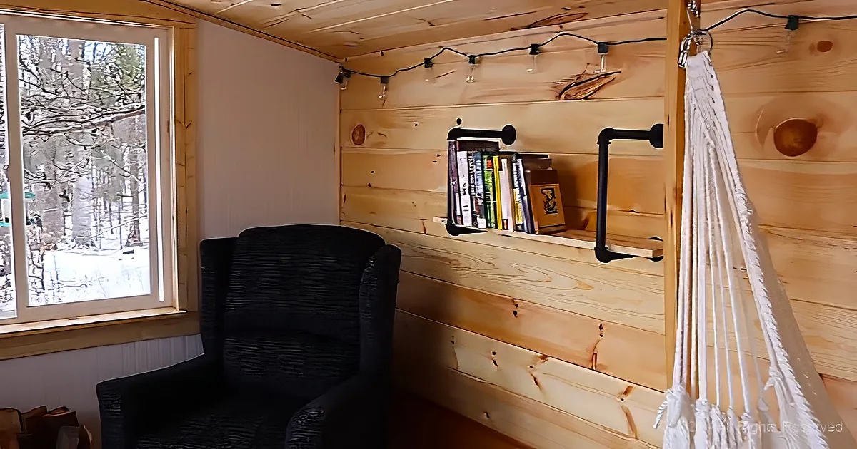 A cozy corner with a black chair, wooden walls, string lights, a bookshelf, and a hammock.