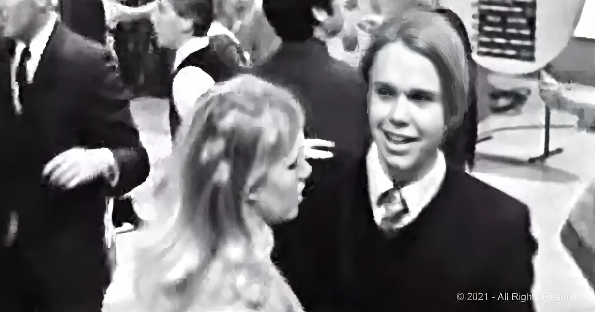 A man in a suit and tie smiles at a woman with long hair in a crowd.