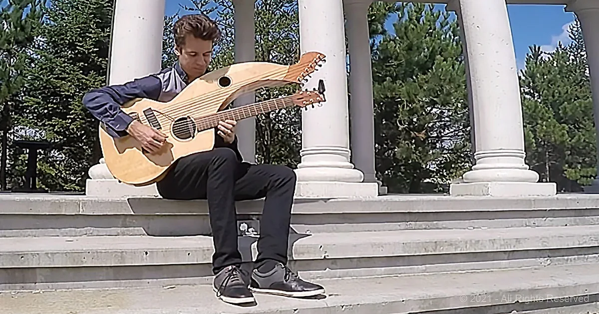 A person sits on steps, playing a unique guitar with a dolphin-like neck.