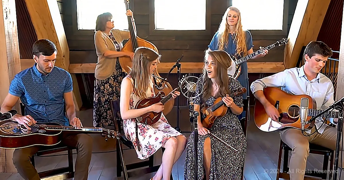A group of musicians, including a singer, play instruments in a cozy indoor setting.