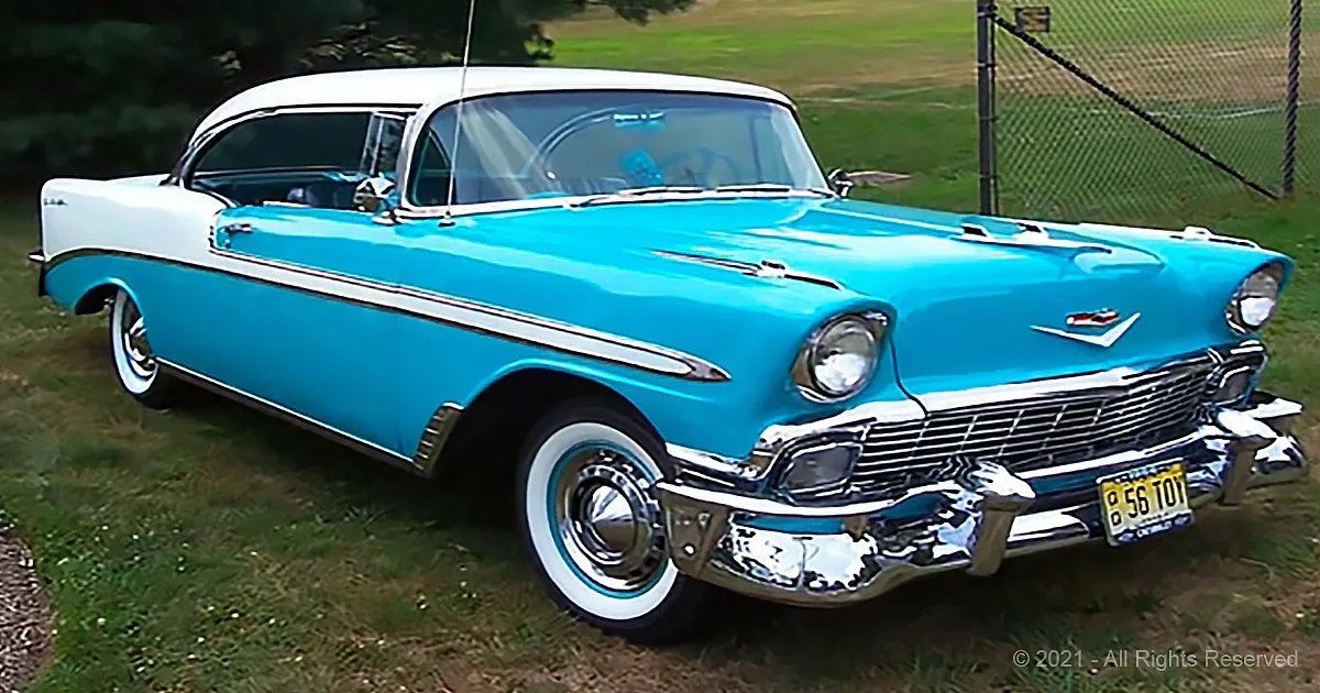 A classic 1956 Chevrolet Bel Air in bright blue with white top and chrome details is parked on grass.