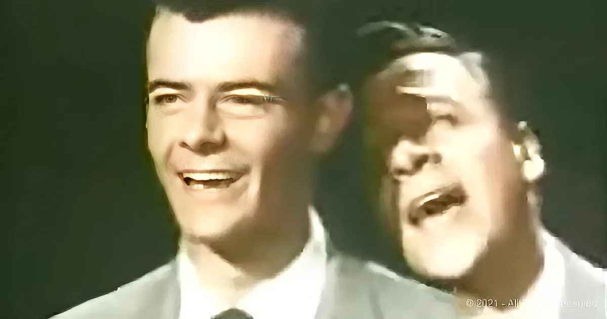 Two men in white shirts, one smiling, the other singing, against a dark background.