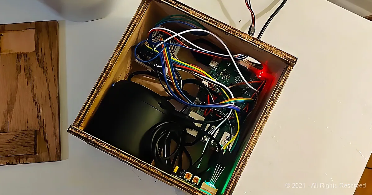 A wooden box contains a Raspberry Pi, colorful wires, and a black device, with a red light indicating power.