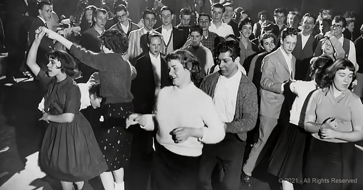 A group of people in 1950s attire are dancing in a crowded room, enjoying themselves.