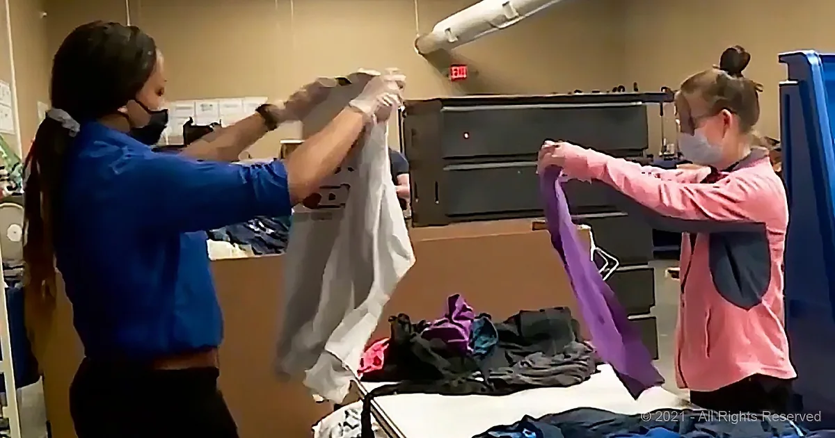 Two individuals in scrubs sort and fold clothes in a medical or healthcare setting.