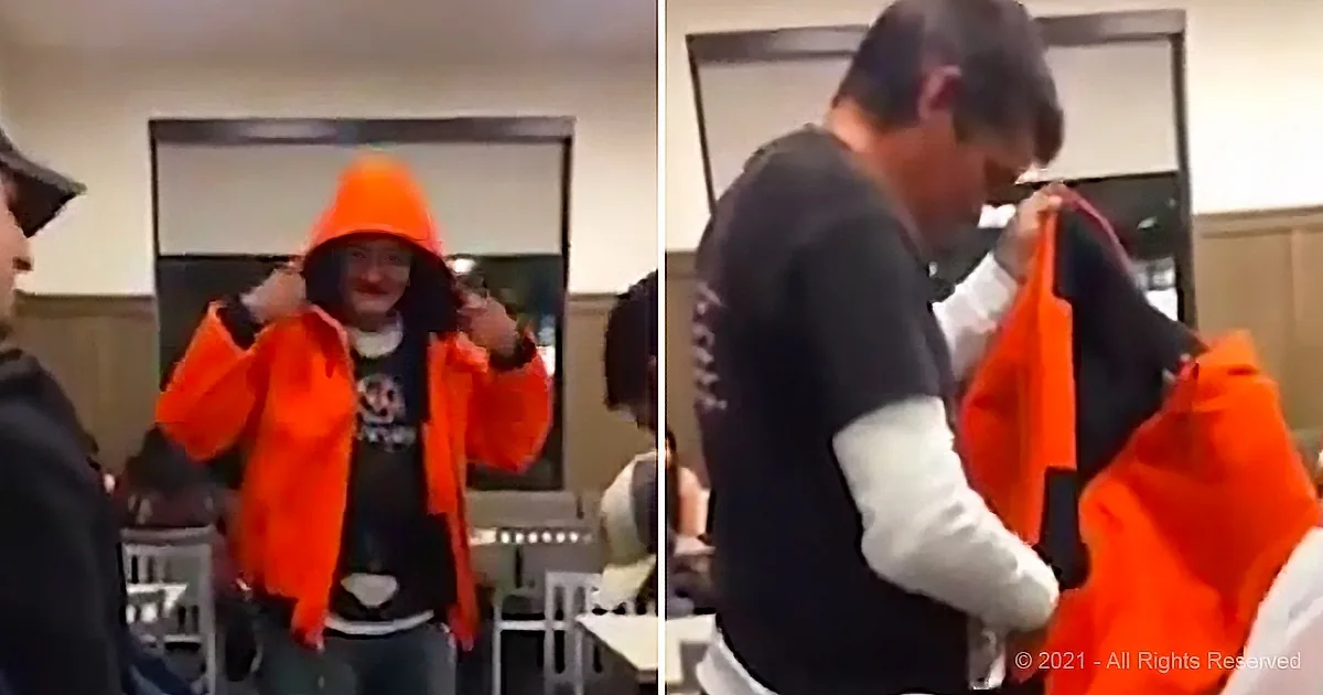 A person in an orange hoodie is adjusting their jacket while another person helps them with it.