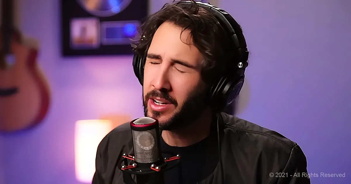 A man with headphones sings into a microphone in a recording studio with a guitar and soft lighting.