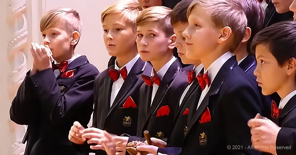 A group of boys in formal attire, including red bow ties, are standing in a row, some holding objects.