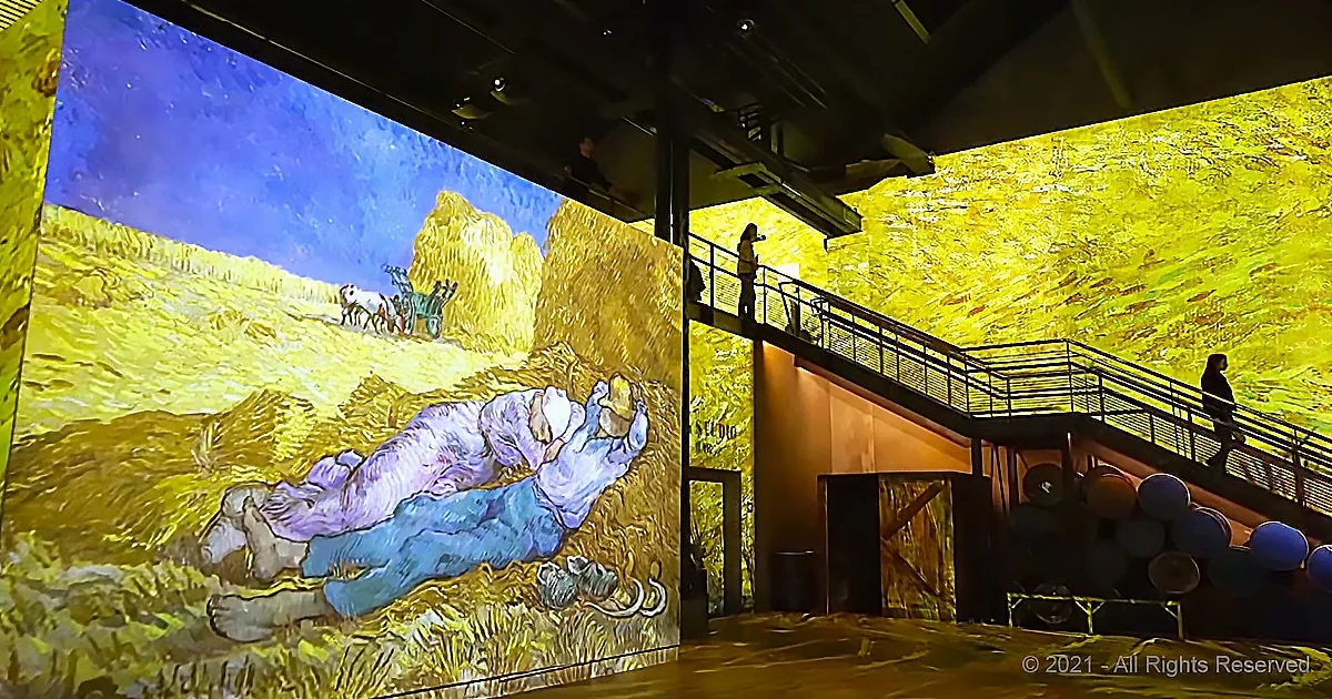 A large projection of a Van Gogh painting of a person lying on the grass is displayed on a wall.