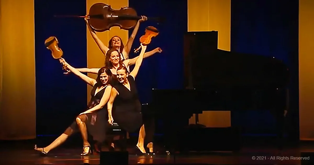 Four women in black dresses perform a synchronized dance with violins and a cello on stage.