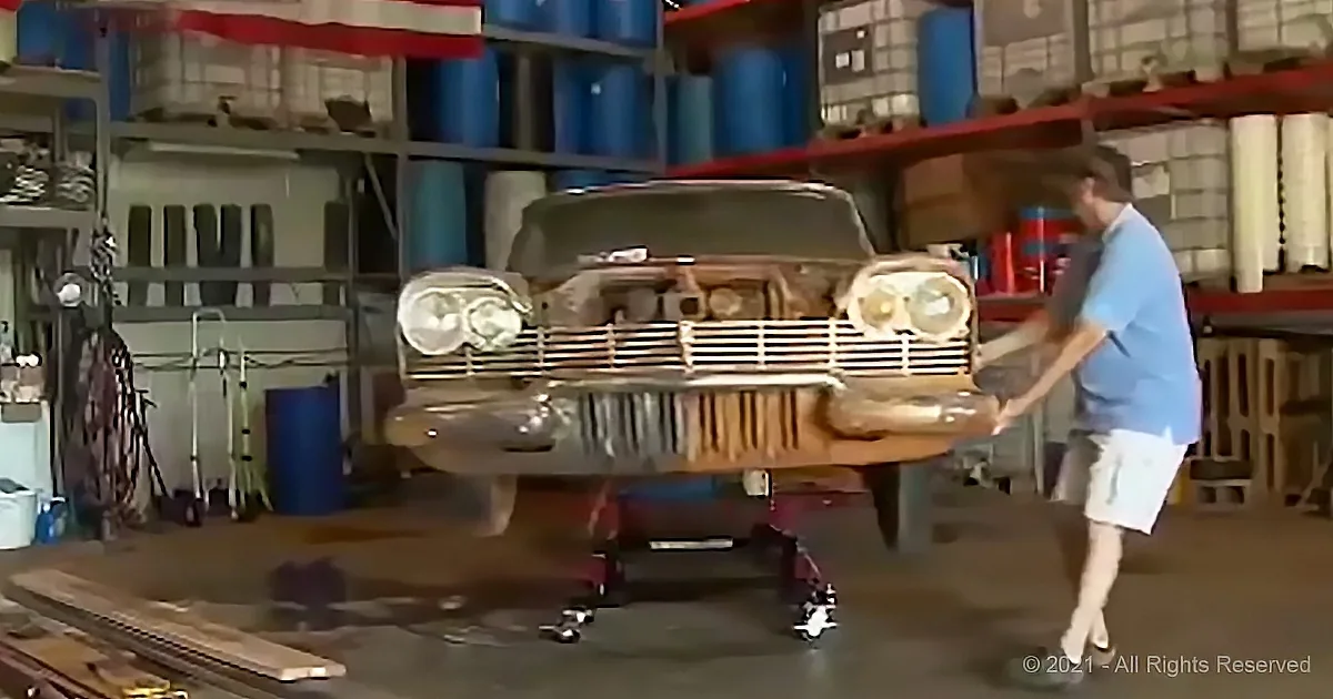 A man works on a vintage car in a garage filled with tools and supplies.