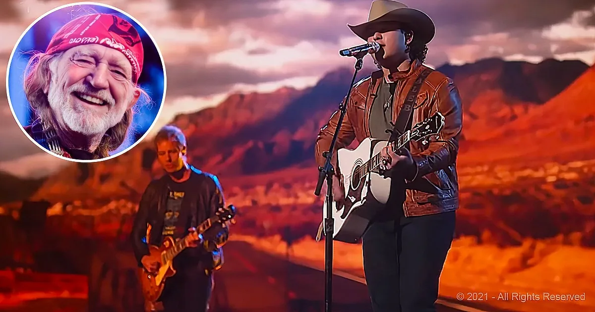 A musician in a cowboy hat plays guitar on stage with a scenic mountain backdrop.