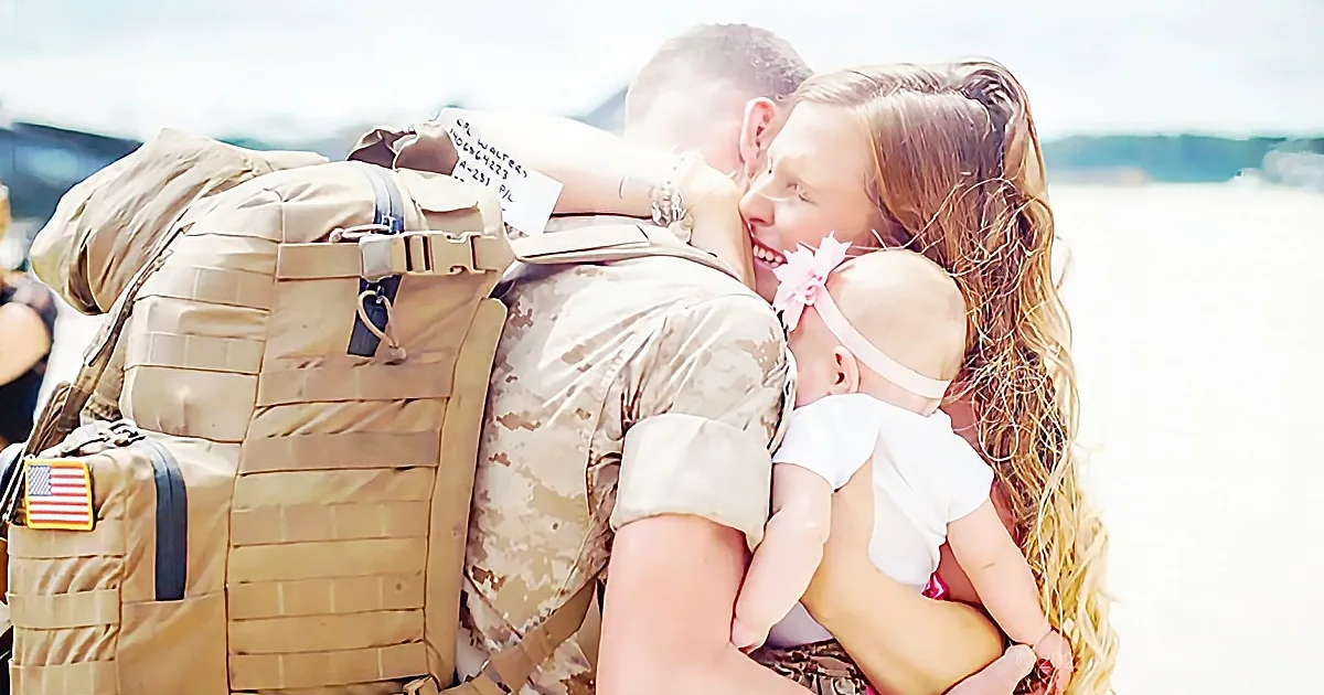 A soldier in uniform embraces a woman and a baby, sharing a tender moment.