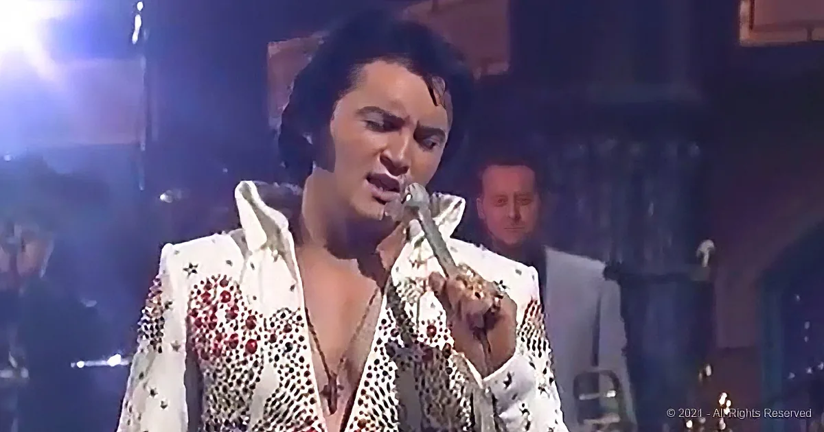 A performer in a glittery white suit sings into a microphone on stage.