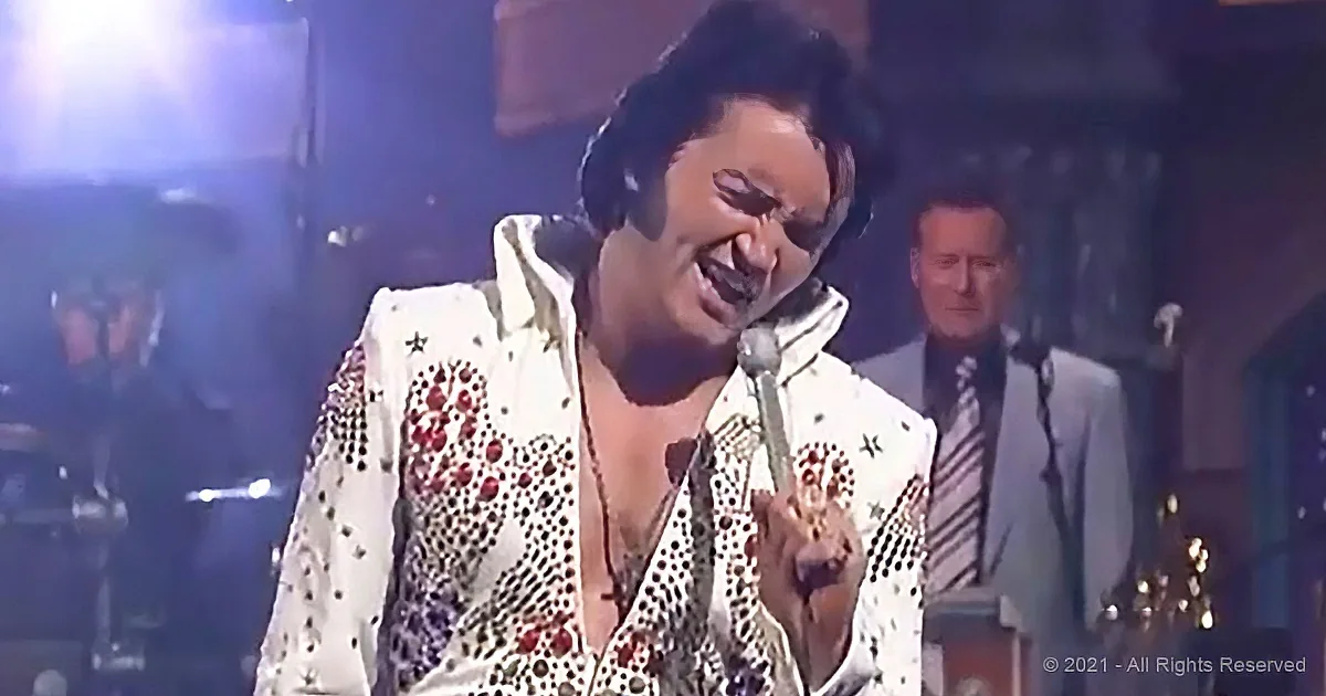 A performer in a white sequined jacket sings into a microphone on stage, with a band in the background.