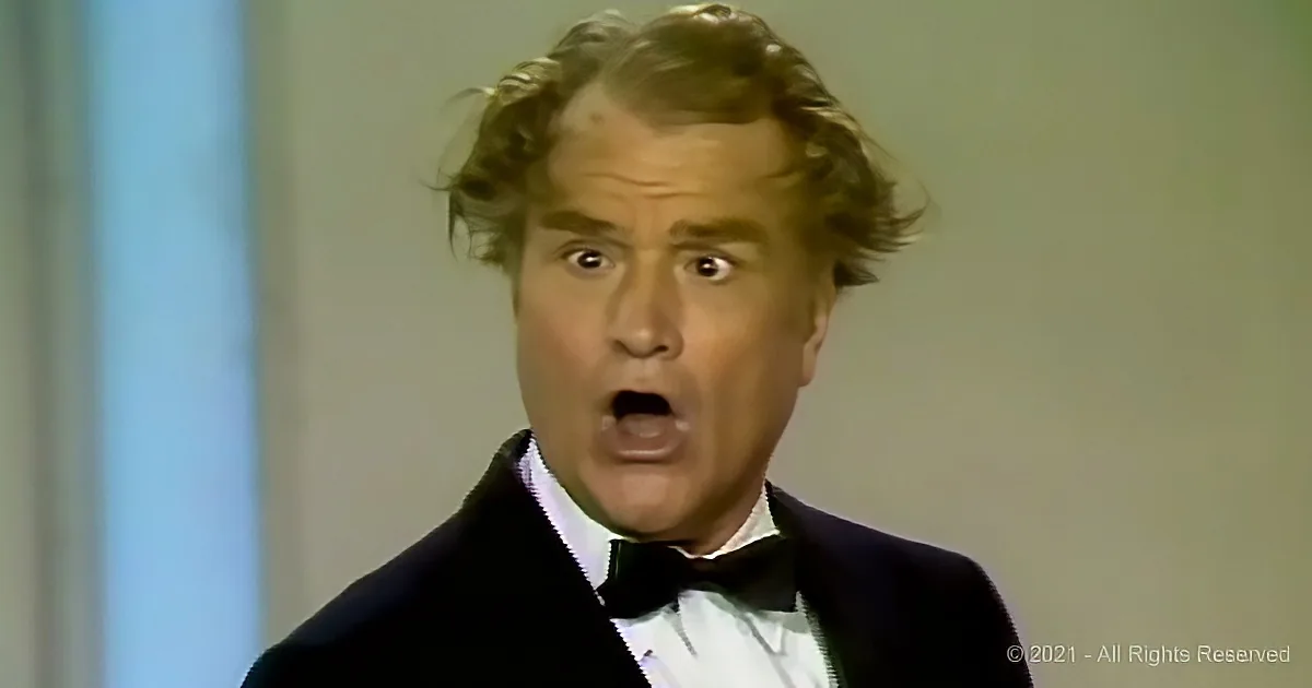 A man in a tuxedo with a surprised expression, mouth open, hair tousled.