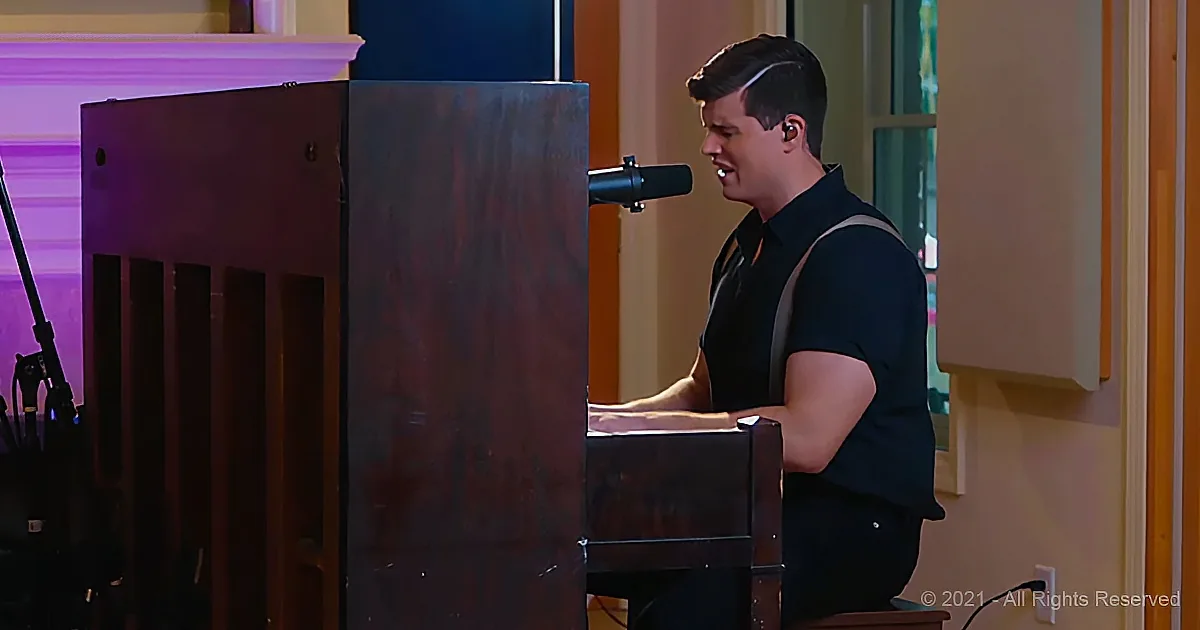 A man in a black shirt sings into a microphone while playing a piano.