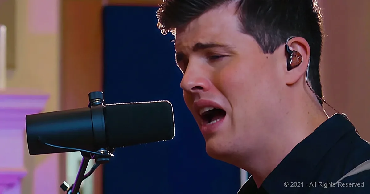 A person singing into a microphone, wearing earphones, with a focused expression.