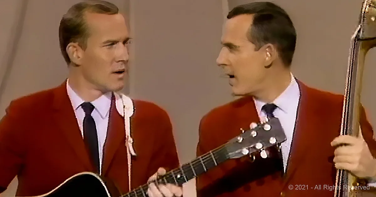 Two men in red suits sing and play guitar, one holding a microphone.