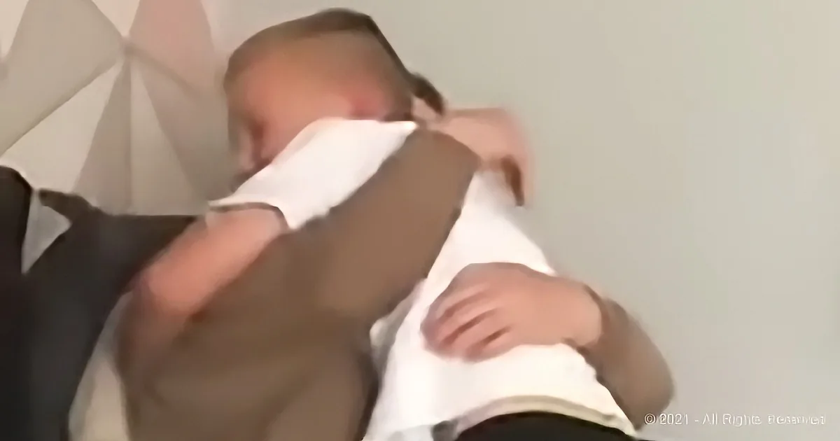 A baby is being held and appears to be sleeping, with a white cloth partially covering its face.