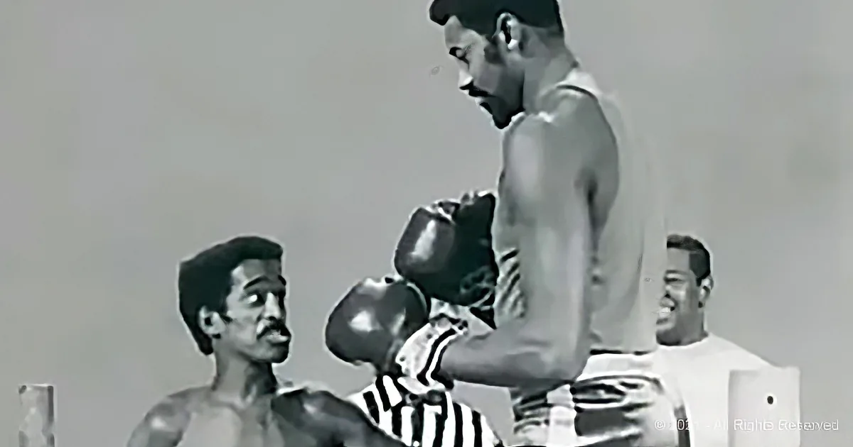 A boxer in a stance, facing another boxer, with a referee in the background.