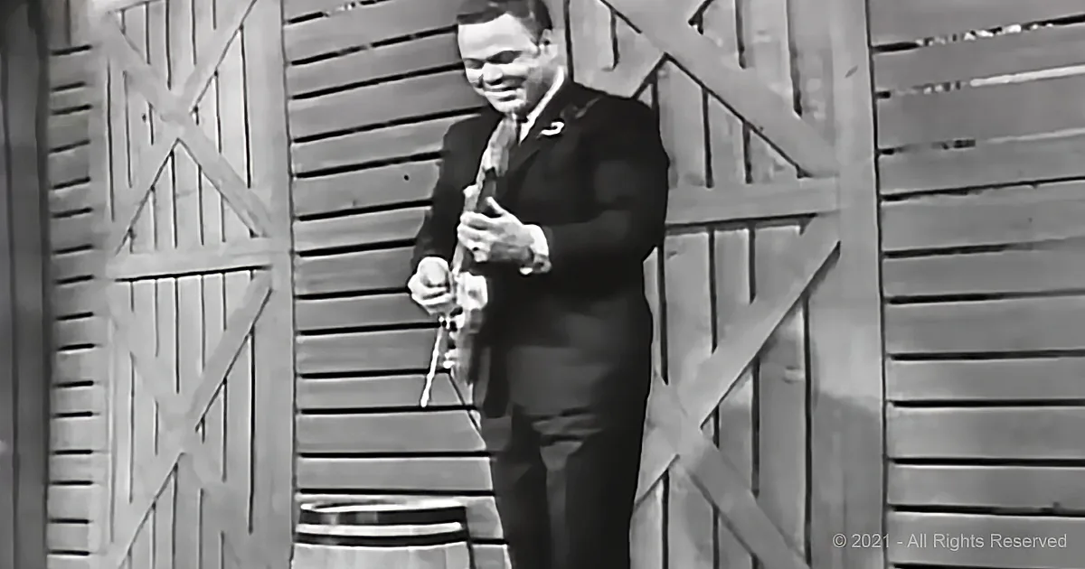 A man in a suit plays a clarinet in front of a wooden backdrop.