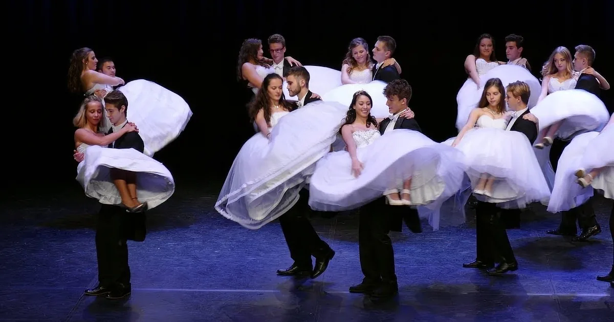 A group of dancers in formal attire performs a synchronized dance routine on stage.