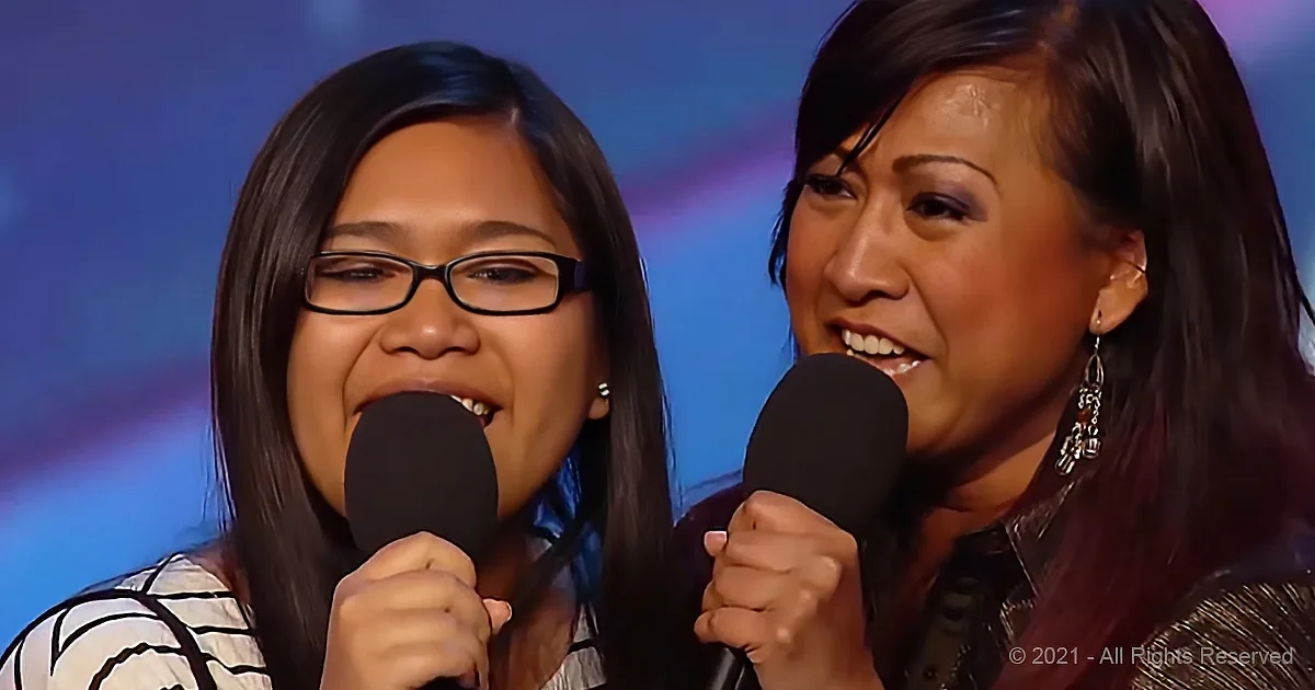 Two women sing into microphones, one with glasses, both smiling and engaged.