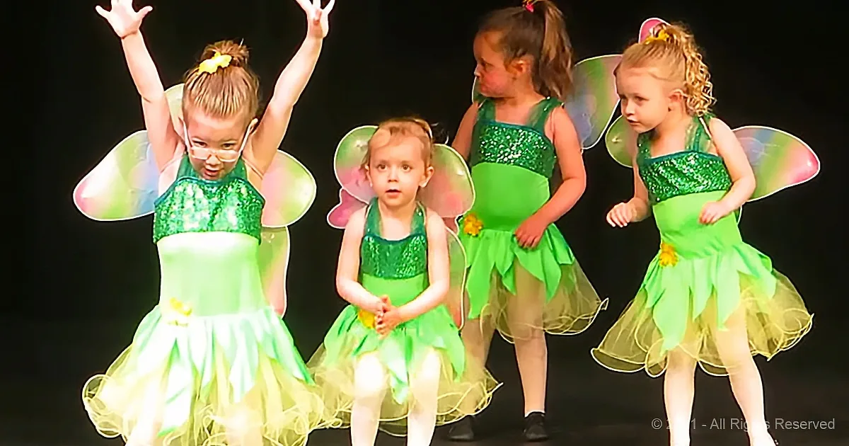 Four children in green fairy costumes with wings, performing on stage.