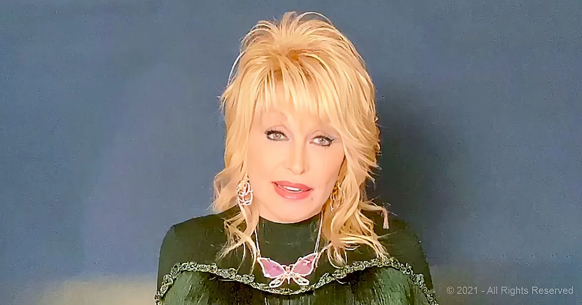 A person with blonde hair and a green outfit with butterfly decorations is shown against a dark background.