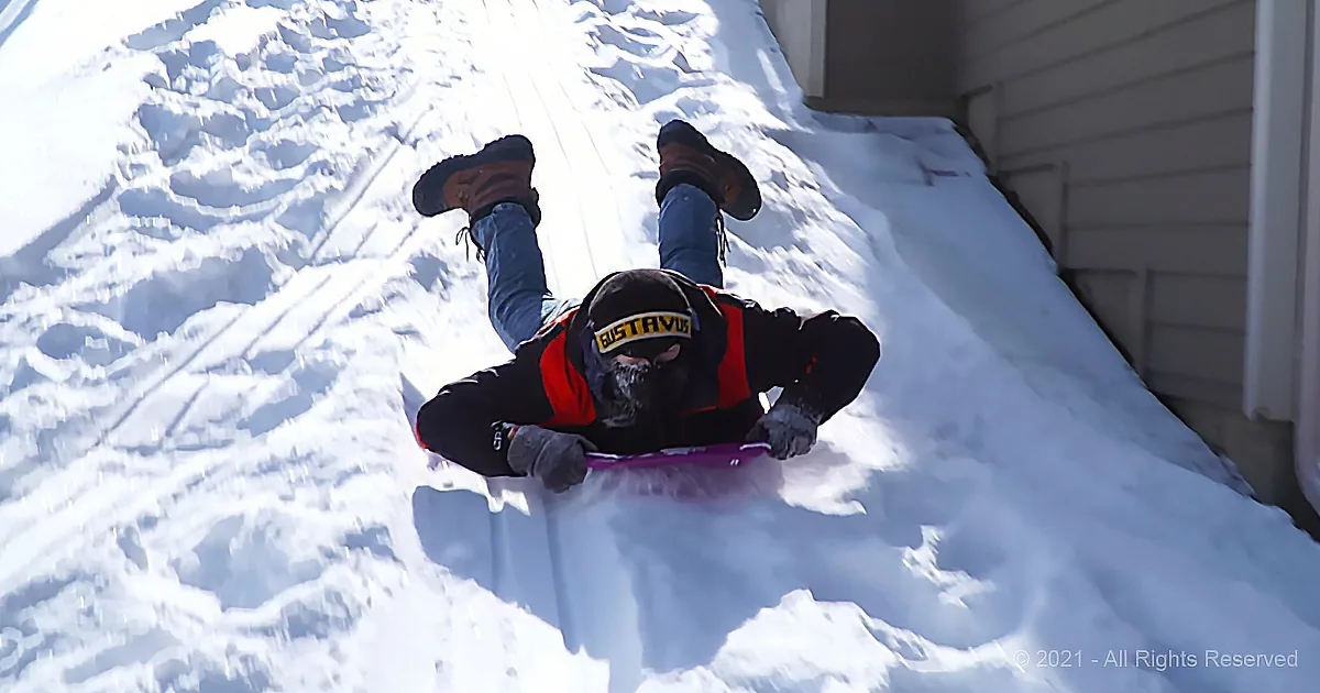 A person wearing a "Gustavus" jacket sleds down a snowy hill.