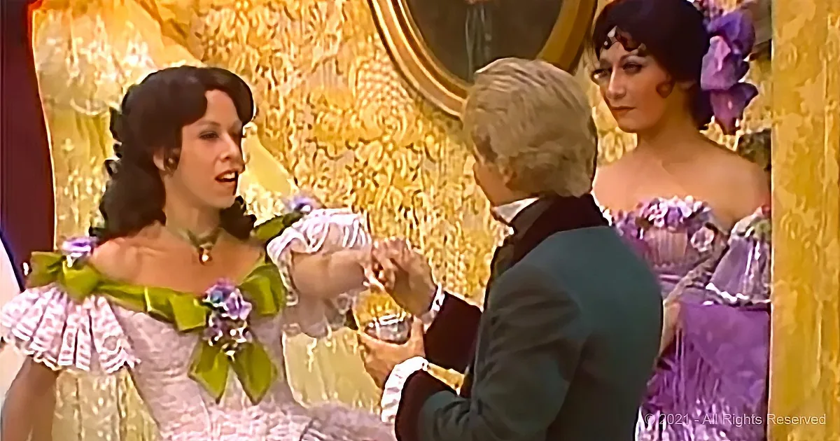 A woman in a green and white dress is holding a small object, possibly a flower, in front of a man in a suit.