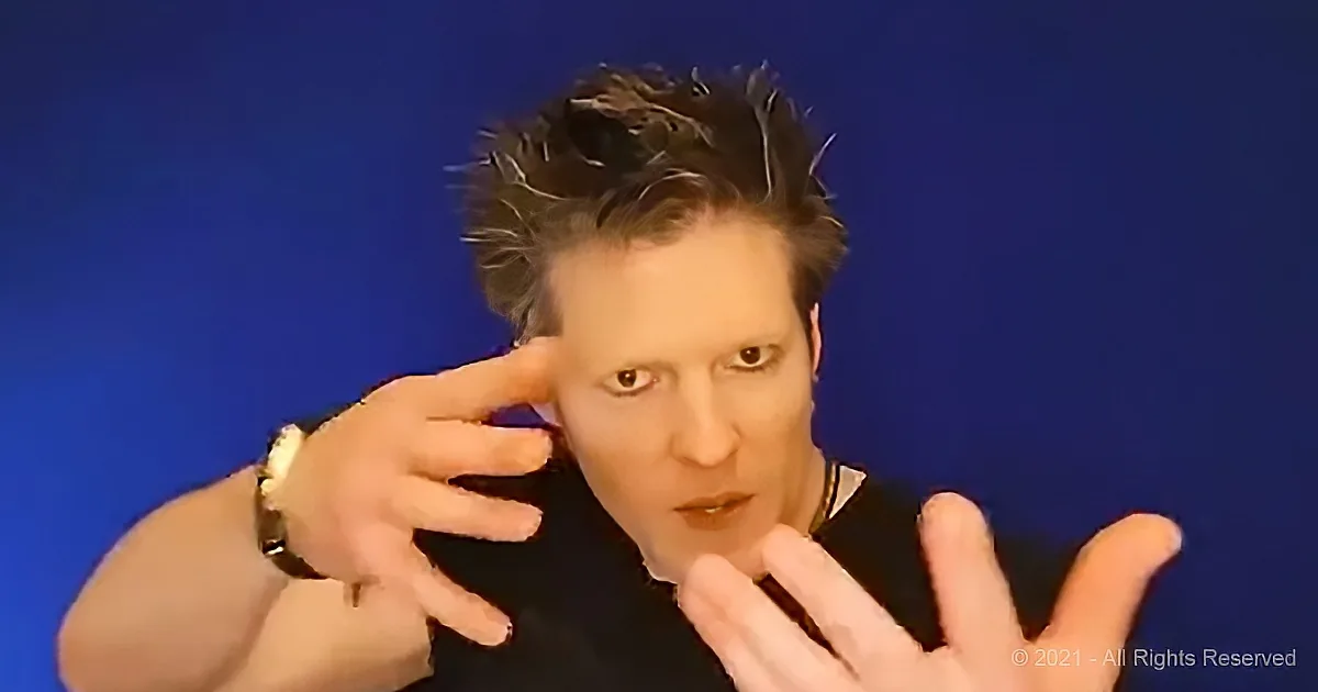 A person with spiky hair, wearing a black shirt and a watch, is making a gesture with their hands against a blue background.