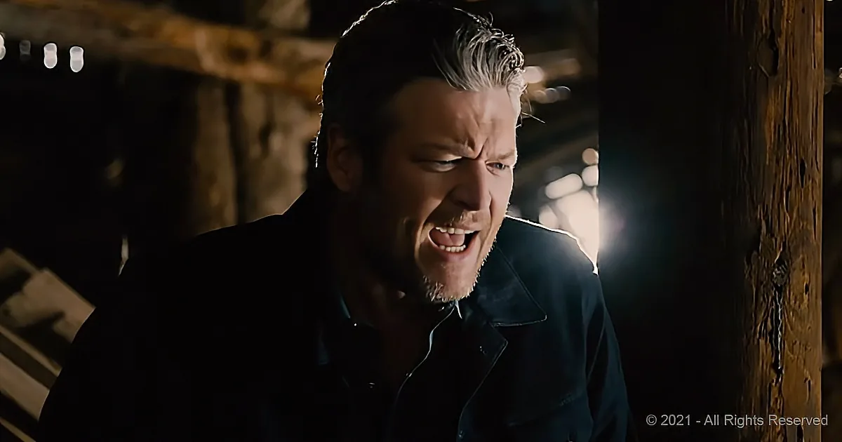 A man with a distressed expression, wearing a dark shirt, stands in a dimly lit, rustic setting.
