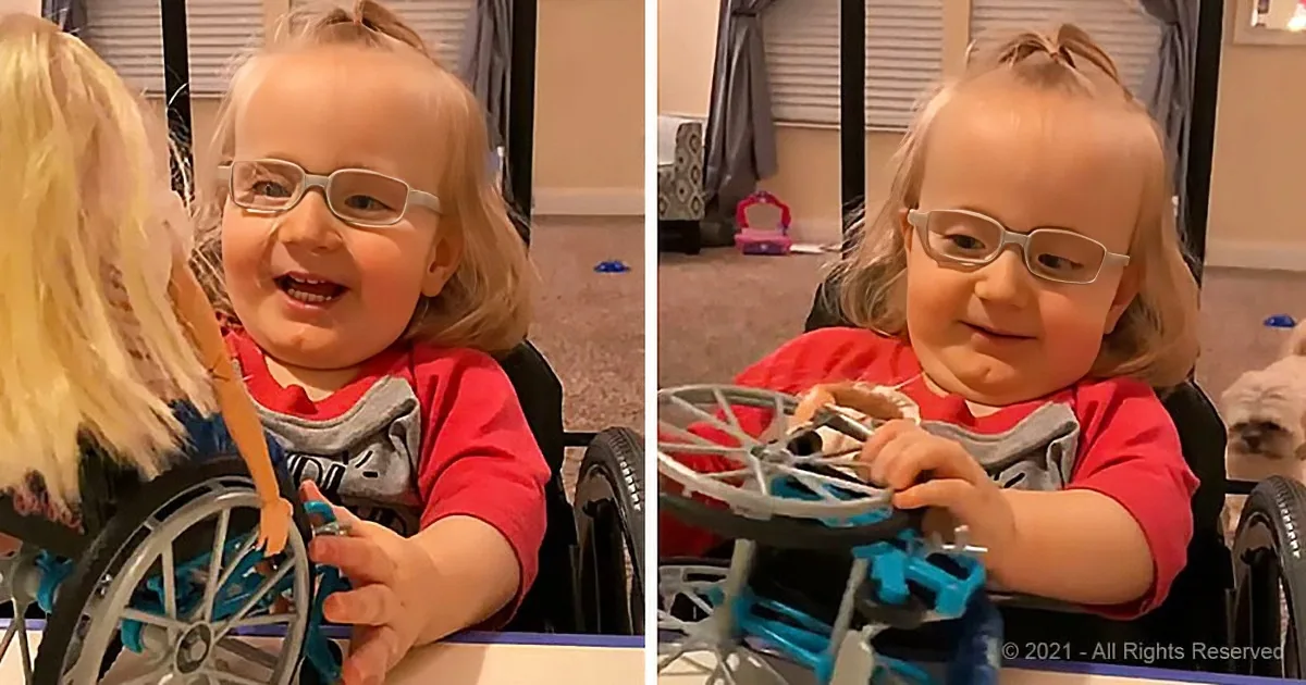 A child with glasses and a red shirt smiles in a wheelchair, interacting with someone off-camera.