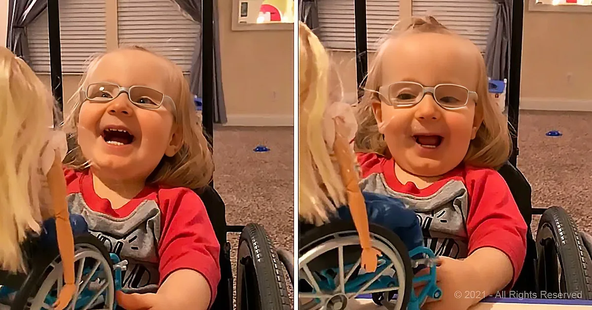 A happy child in a wheelchair smiles widely while holding a doll.