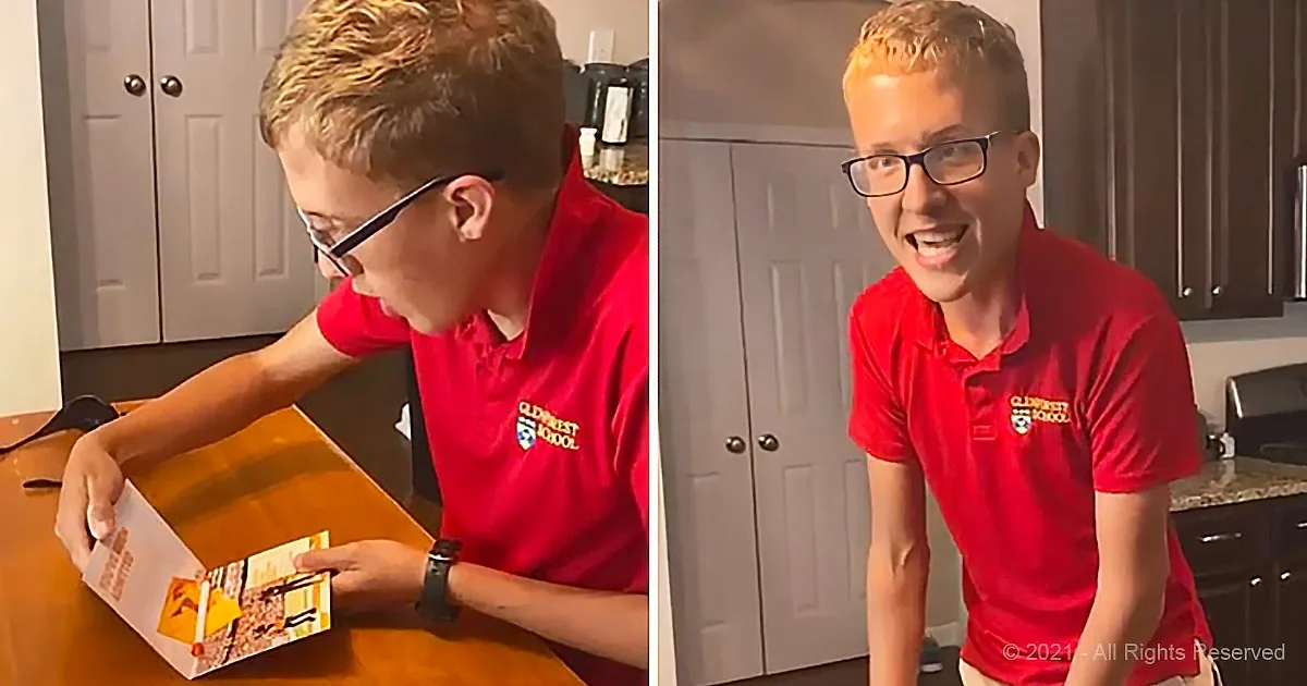 A young man in a red polo shirt is opening a box and smiling in a kitchen setting.