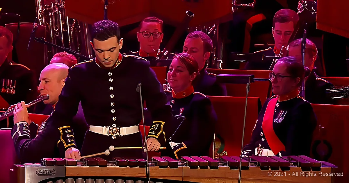 A man in uniform plays the xylophone while a flute player and others in formal attire observe in the background.