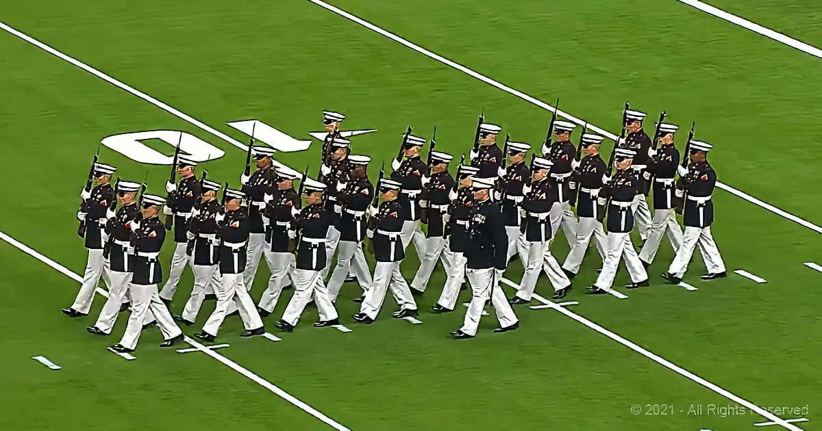A group of uniformed military personnel marching in formation on a green field.