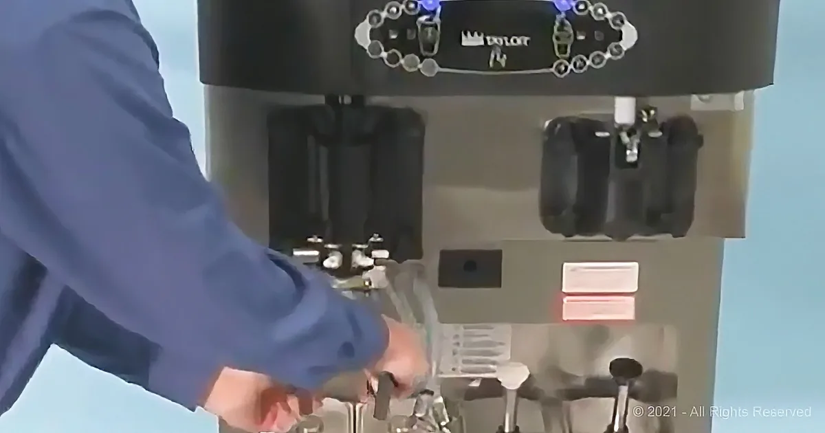 A person in a blue shirt is operating a coffee machine, pouring water into a glass.